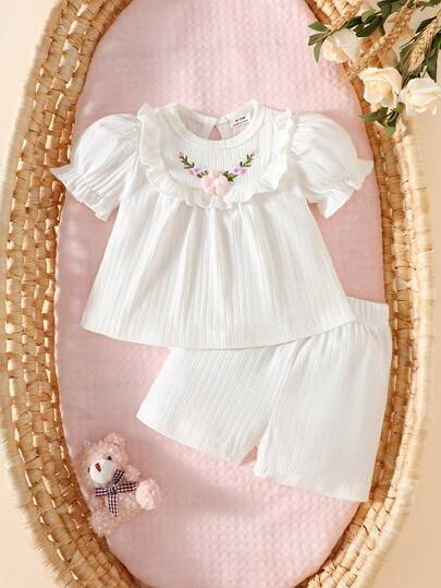 Vit kortärmad topp med broderad tredimensionell blommig blommig design för nyfödd flicka, i kombination med matchande shorts. Tyget är enkelt, bekvämt och hudvänligt, lämpligt för familjepresenter på sommaren.