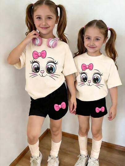 2件套女童时尚可爱蝴蝶结小猫印花圆领短袖T恤上衣和短裤套装，杏色上衣搭配黑色短裤，适合春夏休闲外出穿着。