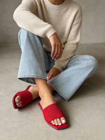 Sandalias planas estilo slide, modelo minimalista de punta cuadrada, tono rojo vibrante, banda ancha de material textil elástico con textura acanalada, plantilla ergonómica delgada de acabado mate coordinado, estructura ligera de diseño abierto para máxima frescura y comodidad, suela flexible en tono neutro con borde delgado y reborde discreto, estilo moderno y versátil ideal para outfits relajados, looks de verano o atuendos que buscan resaltar con un acento de color en los días cálidos