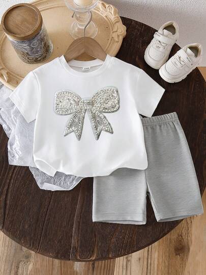SHEIN Playful Pals 女婴夏季套装，白色T恤饰有水钻蝴蝶结印花，搭配浅灰色休闲短裤，宽松舒适。整体造型清新可爱，为孩子增添甜美气息。