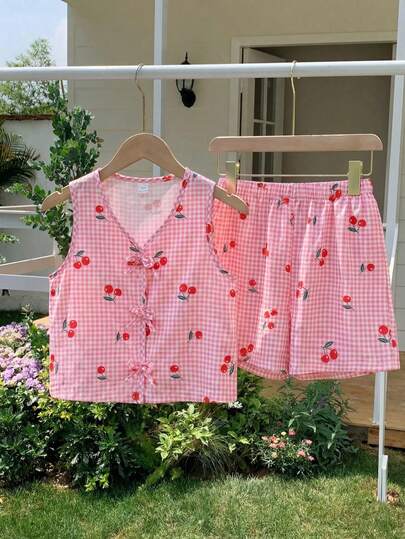SHEIN Detta är ett set för tjejer, bestående av två delar: en ärmlös tröja med digitaltryck i rosa rutmönster och körsbärsmotiv, samt löst sittande shorts. Tröjan har en rosettdekoration och shortsen har en resår i midjan. Perfekt för tjejer i sommar.