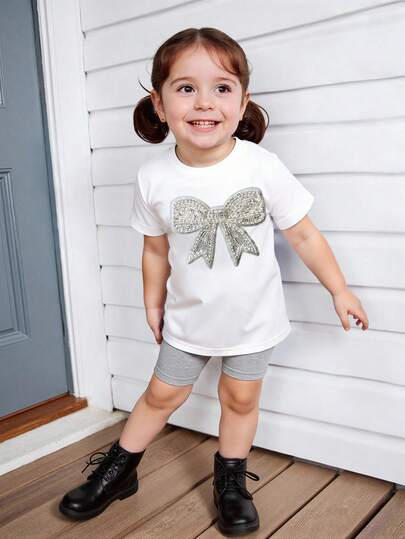SHEIN Playful Pals Baby Girls' Summer Outfit, White T-Shirt With Rhinestone Bow Print, Paired With Light Gray Casual Shorts, Loose And Comfortable. The Overall Look Is Fresh And Cute, A Sweet Element For Children .