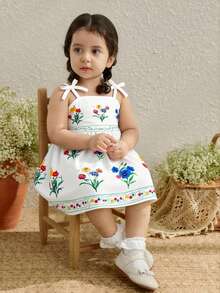 SHEIN Vestido avental infantil com estampa floral, tecido leve e macio, alças com laço, estampa floral colorida, amarração na cintura, modelagem solta e fluida, ideal para piqueniques ao ar livre, brincadeiras no jardim e para a primavera/verão. - Branco - Ver 6