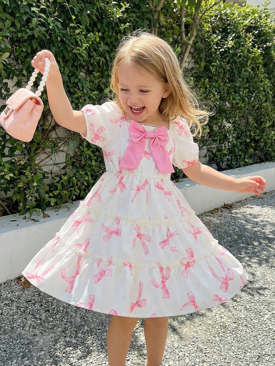 Elladie kids Đầm kiểu bánh kem 3D dễ thương cho bé gái, đầm đồng phục học sinh, thân đầm màu be nhạt, in họa tiết nơ hồng, cổ vuông, tay ngắn phồng, nơ hồng lớn trang trí ngực, viền bèo nhiều lớp, ngọt ngào và đáng yêu, toát lên vẻ ngây thơ của trẻ nhỏ. - Nhiều màu - Xem 1