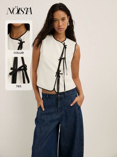 Nöista Top sin mangas blanco con ribete negro y adornado con lazos negros estilosos a lo largo del frente, con una silueta ajustada perfecta para el otoño. Casual, oficina, vuelta al colegio, concierto y estilo bohemio