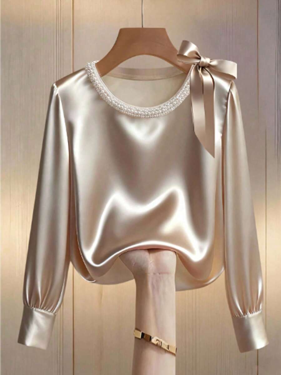 Franclia 这款女士优雅缎面圆领针织衬衫饰有珍珠滚边，宽松的杏色缎面长袖，尽显法式优雅，是约会和打造迷人造型的完美之选。肩部饰有可爱的蝴蝶结，适合日常穿着，尤其适合春秋两季。冬季、圣诞节、新年、白色新年夜、派对、海滩、浪漫、休闲、情人节、约会、毕业季等场合皆宜，也是时尚通勤、商务办公、百搭时尚日常休闲以及都市教师职业装的理想之选。 - 杏色 - 查看 1