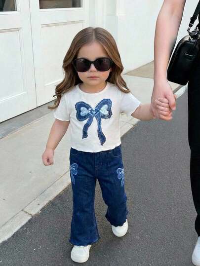 SHEIN Este conjunto de 2 piezas para bebé niña con estilo minimalista casual y retro americano presenta una camiseta de manga corta de cuello redondo minimalista de color azul oscuro y shorts con un diseño de parches de encaje y lazo, perfecto para un look relajado de verano.