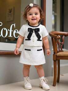 SHEIN Conjunto de 2 piezas para niña bebé: blusa de tweed tejido con botones de perlas falsas y decoración de lazo, talla grande una falda - Elegante conjunto de 2 piezas para uso diario, estilo francés elegante y señorial, de vuelta al colegio, atuendos estilosos, combinación a juego mamá e hija. Conjunto de 2 piezas para niña bebé de estilo vintage blanco para niña de 2 años, uniforme escolar para niña - Blanco - Ver 1