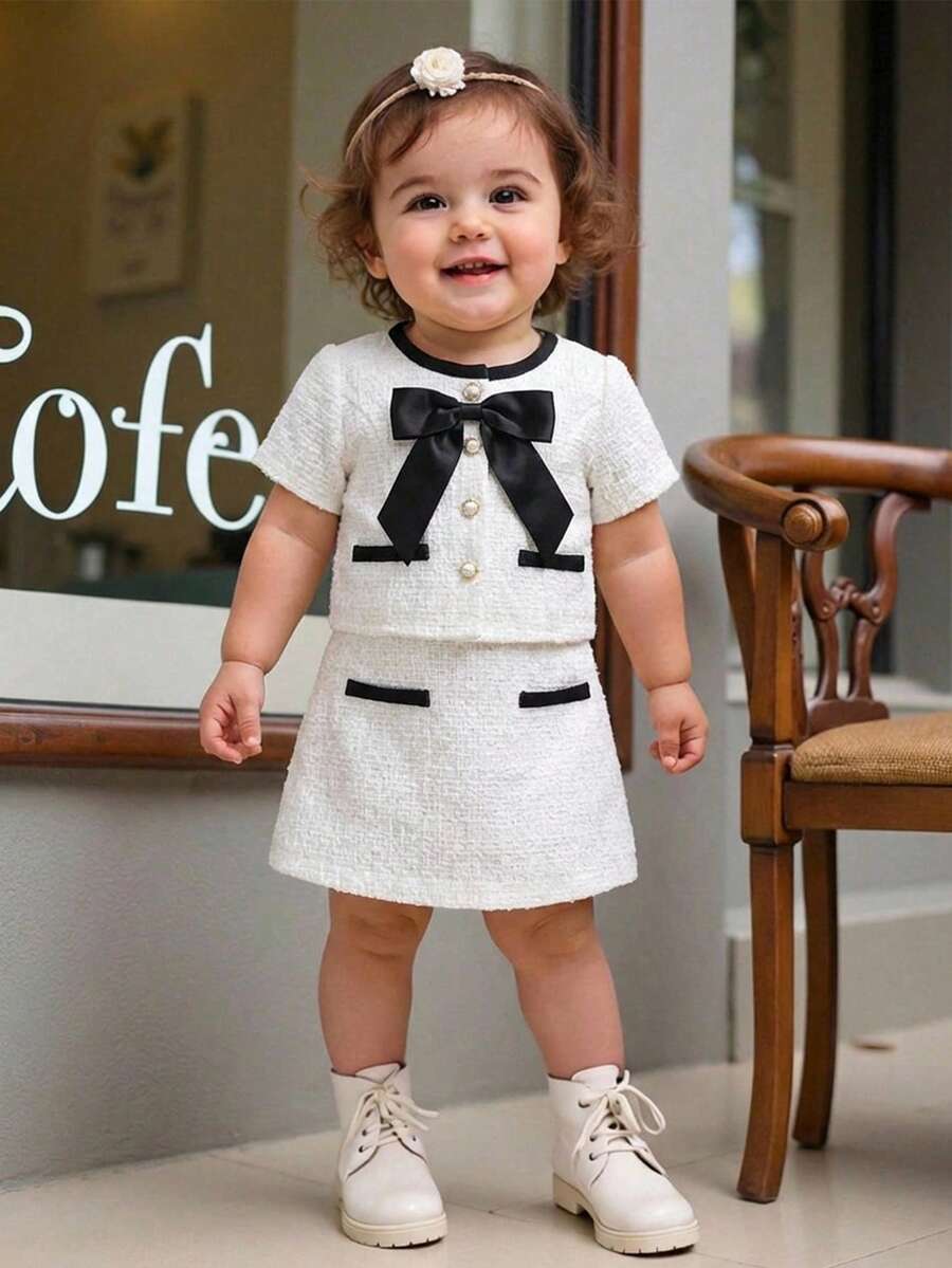 SHEIN Conjunto de 2 piezas para niña bebé: blusa de tweed tejido con botones de perlas falsas y decoración de lazo, talla grande una falda - Elegante conjunto de 2 piezas para uso diario, estilo francés elegante y señorial, de vuelta al colegio, atuendos estilosos, combinación a juego mamá e hija. Conjunto de 2 piezas para niña bebé de estilo vintage blanco para niña de 2 años, uniforme escolar para niña - Blanco - Ver 1