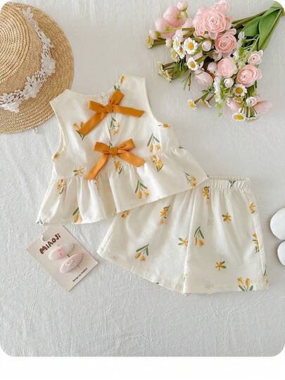 Bộ đồ bé gái dễ thương đi nghỉ mát, gồm áo hai dây và quần cạp chun họa tiết hoa, trang trí nơ.