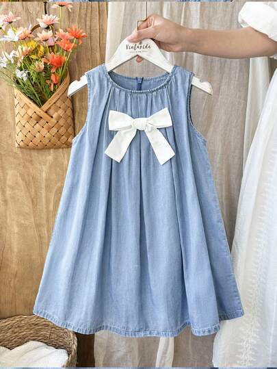 女童浅蓝色牛仔无袖连衣裙，复古可爱休闲校园风，正面饰有3D白色蝴蝶结，褶皱设计增添俏皮感，宽松版型，后背隐形拉链方便穿脱，舒适清爽，适合春夏穿着，搭配凉鞋，打造轻松甜美造型。
