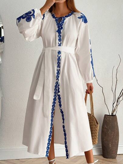 Damska, swobodna, biała sukienka midi z paskiem i niebieskim haftem, długimi rękawami typu dolman i wiązaniem przy szyi