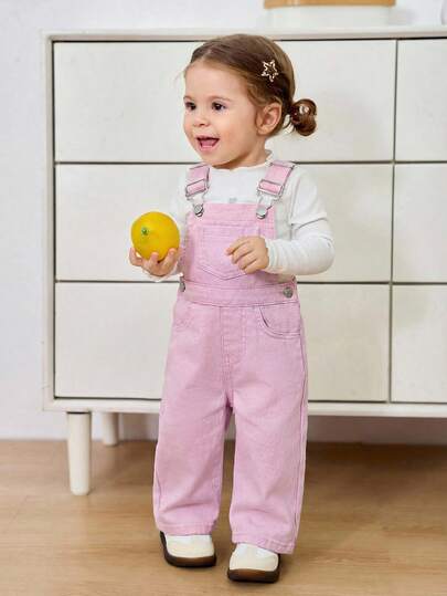 Bộ quần yếm denim in hình bò sữa cho bé gái, có nơ trang trí, dáng rộng.