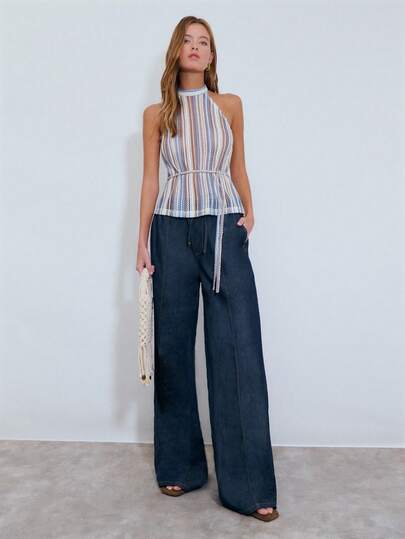 Nöista 这款优雅的度假风上衣采用立领和挂脖设计。无袖剪裁、竖条纹、舒适的钩编面料、多种自然色调以及收腰系带是其主要设计亮点，使其适合夏季度假和日常通勤。