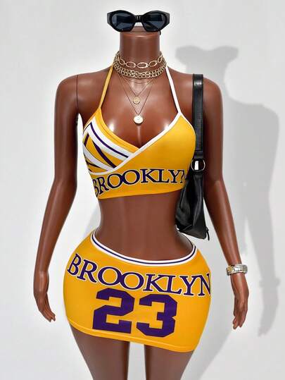 BamGleam Bộ đồ hè mới về: Áo croptop cổ yếm in chữ và số màu vàng & tím tương phản + chân váy mini vạt lệch, trang phục hở lưng gợi cảm cho xem World Cup / đi club lễ hội âm nhạc, phong cách thể thao Mỹ.