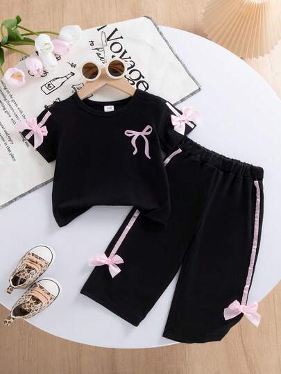 SHEIN طقم بنطلون وتي شيرت للبنات الصغار، التي شيرت بياقة دائرية باللون الأسود مزين بفيونكة وطباعة وردية على الصدر، وأكمام مزينة بفيونكة وردية، مناسب للمدرسة والاستخدام اليومي