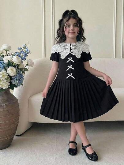 女童黑色蕾丝领拼接短袖连衣裙，饰有单个蝴蝶结，拼接褶裥下摆，时尚舒适，适合日常穿着。