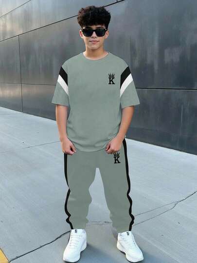 Conjunto informal minimalista de estilo universitario para niño preadolescente, con camiseta de manga corta de cuello redondo suelta y cómoda con bloqueo de color, estampado de corona, letras en inglés y diseño deportivo, adecuado para primavera y verano, y pantalones a juego.