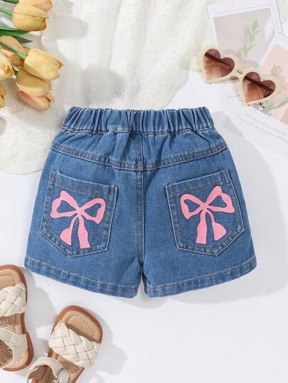 女婴牛仔短裤套装（2件套），夏季新品，休闲可爱，中蓝色牛仔布，夏季度假，不规则裙裤设计，三粒扣装饰，松紧腰带，蝴蝶结印花，宽松版型，柔软棉质牛仔面料，百搭日常T恤，适合夏季度假、日常外出、聚会等场合。