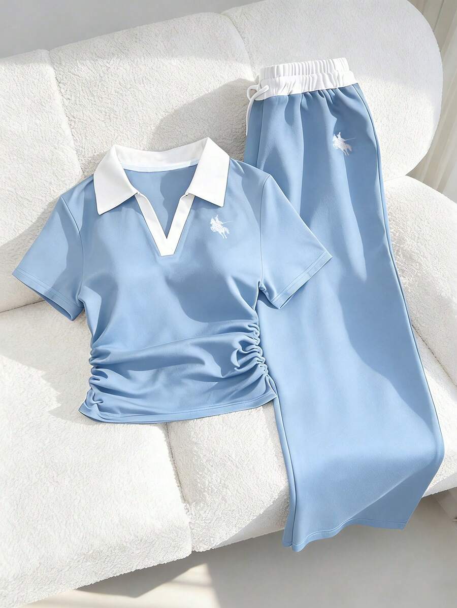 Bộ đồ thể thao thường ngày dành cho nữ tuổi teen, gồm áo polo cổ bẻ với đường chỉ tương phản, thêu ngực, áo tay ngắn cạp xếp ly và quần ống rộng có dây rút. Bộ đồ thể thao màu xanh navy này cân bằng hoàn hảo giữa sự thoải mái và phong cách. Tinh tế nhưng không phô trương, quần ống rộng cạp điều chỉnh được và cổ áo polo tương phản giúp tôn lên đường nét cổ. Một bộ trang phục mùa hè thiết yếu để thư giãn, tập luyện hoặc mặc ngoài trời. - Màu xanh lam - Xem 1