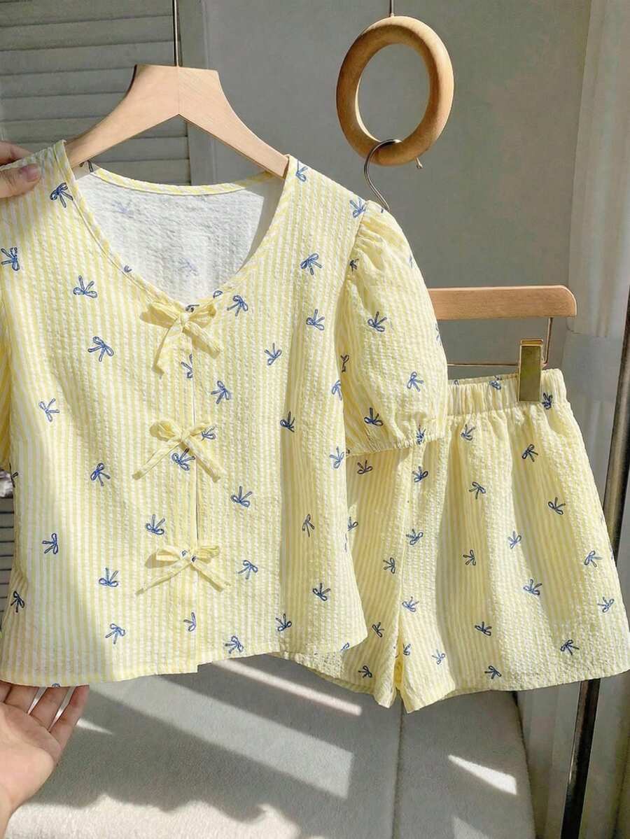 Sparklyn Bộ áo sơ mi cổ chữ V cho bé gái tuổi teen, điểm nhấn là những chiếc nơ cùng màu ở cổ áo và nẹp áo, tay áo ngắn phồng tạo nên vẻ ngọt ngào. Kết hợp với quần short rộng rãi cùng chất liệu, tạo nên phong cách giản dị và thoải mái, phù hợp để mặc ở nhà hoặc ngoài trời vào mùa hè. - Màu vàng - Xem 1
