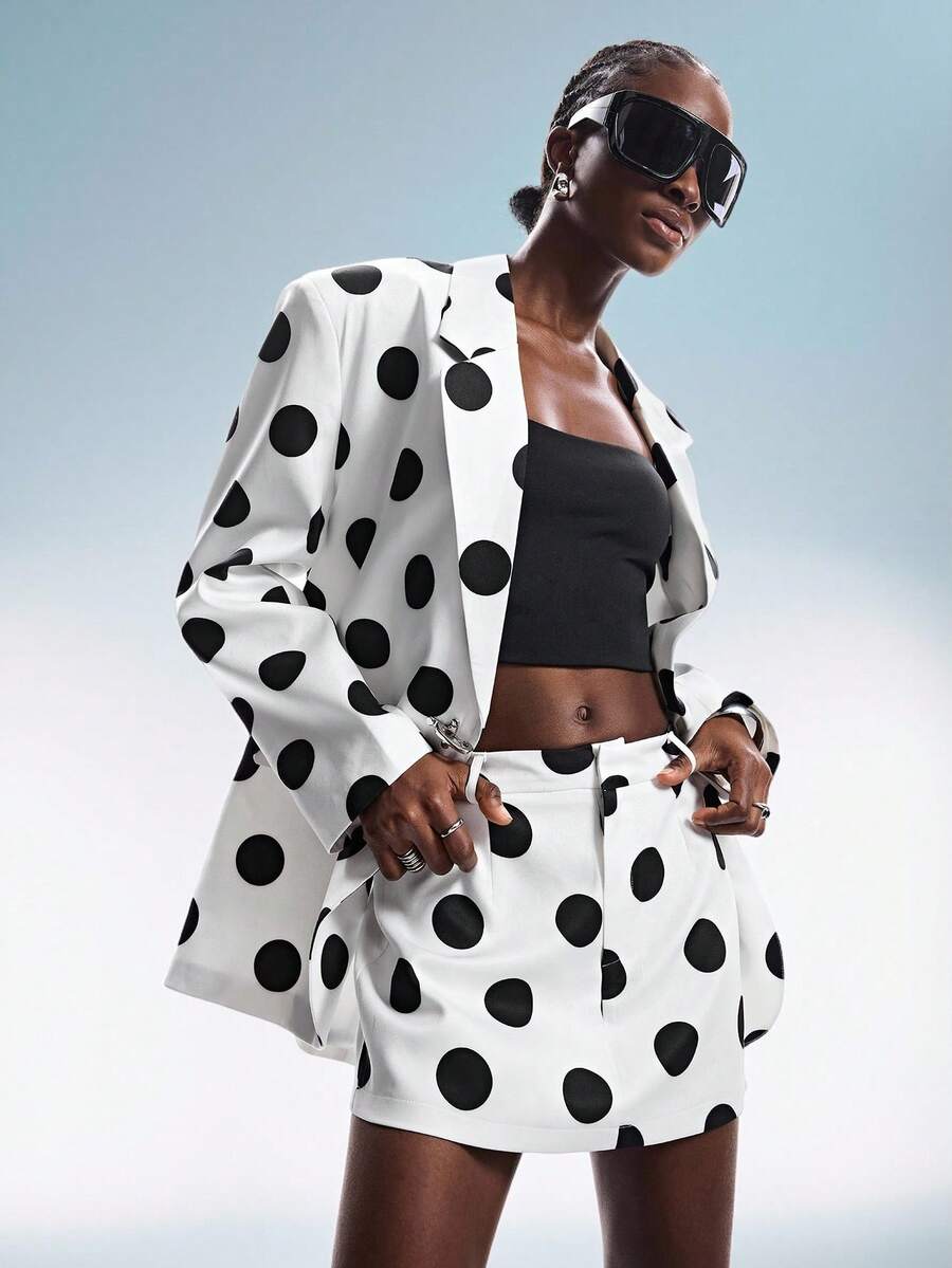 GENKIRA Bộ vest nữ dáng rộng hiện đại pha chút cổ điển, họa tiết chấm bi đen trắng tương phản, gồm áo blazer và chân váy ngắn. Thiết kế bất đối xứng với ve áo, túi nắp và khuy kim loại. Phong cách punk, avant-garde, retro, cá tính, năng động, phù hợp cho công sở. - trắng - Xem 1