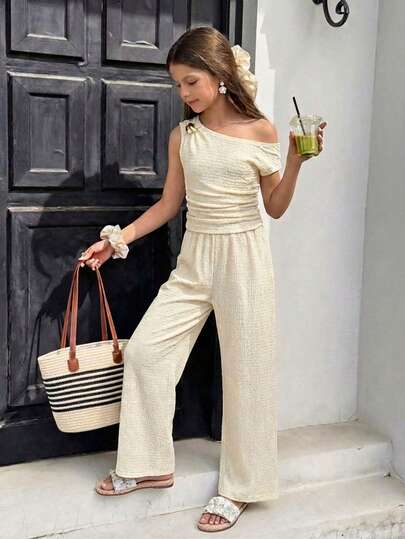 Bộ đồ cho bé gái tuổi teen: Áo thun có thiết kế vai bất đối xứng, một bên được đỡ bằng dây mảnh và bên còn lại buông tự nhiên để lộ vai, tạo nên vẻ gợi cảm nhẹ nhàng. Phần eo được xếp ly giúp tôn dáng, rất phù hợp để mặc vào mùa xuân và mùa hè.