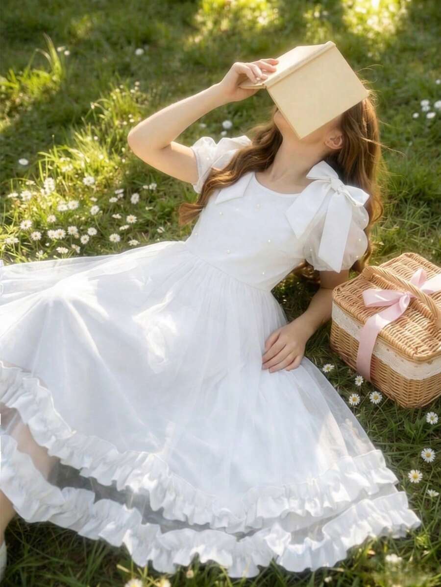 SHEIN Đầm xanh thanh lịch cho bé gái. Đây là chiếc đầm kiểu công chúa phù hợp cho bé mặc hàng ngày, dự tiệc sinh nhật, biểu diễn piano, làm phù dâu trong đám cưới và các dịp khác. Đầm được làm từ chất liệu chiffon màu xanh, có nơ lớn trang trí trên vai, tay phồng, đính ngọc trai khắp thân đầm và chân váy xếp tầng nhiều lớp, làm nổi bật phong cách tinh tế và đáng yêu. Đây là lựa chọn phổ biến cho bé mặc hàng ngày hoặc trong các dịp trang trọng. - trắng - Xem 1