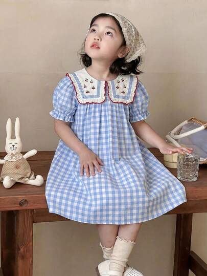 SHEIN Vintaside Kids Đầm mùa hè kẻ caro xanh trắng cho bé gái, cổ áo thêu hình quả anh đào, tay phồng và chân váy xòe rộng, tươi tắn và dễ thương, phù hợp cho trang phục mùa hè. Họa tiết kẻ caro mang đến nét cổ điển, đầy đủ các yếu tố ngọt ngào.