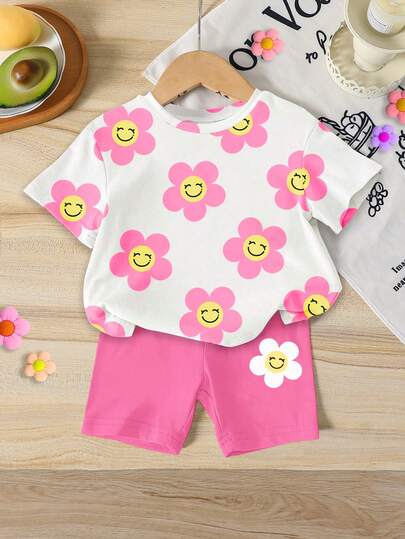 Bộ 2 món cho bé gái gồm áo tay ngắn cổ tròn in hình hoa hướng dương và mặt trắng, và quần short ôm sát in hình hoa hướng dương màu hồng cánh sen, thích hợp cho mùa hè đi học, ở nhà, dã ngoại, bộ đồ hè dễ thương cho bé gái, phong cách Hàn Quốc.