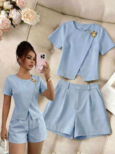 Conjunto de dos piezas para mujer con top de manga corta de diseño cruzado y detalle de broche dorado, combinado con pantalones cortos de talle alto con plisados, ideal para looks elegantes y casuales de oficina o uso diario