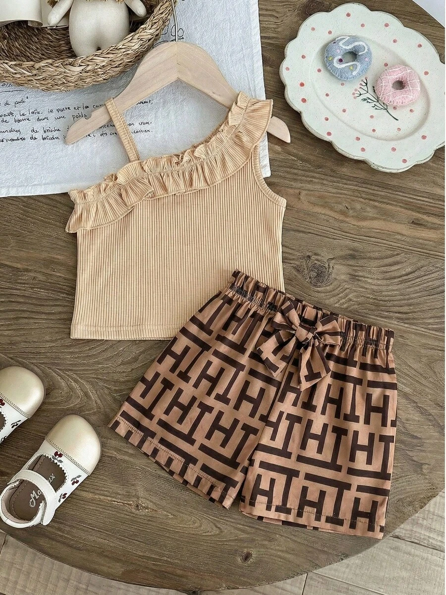 Bộ trang phục mùa hè cho bé gái, gồm áo lệch vai có bèo nhún và quần short in họa tiết hoa hình học. Điểm nhấn là chiếc nơ cùng màu ở eo, tạo nên vẻ ngoài ngọt ngào nhưng vẫn sành điệu cho những chuyến đi chơi năng động. - Màu Khaki - Xem 1