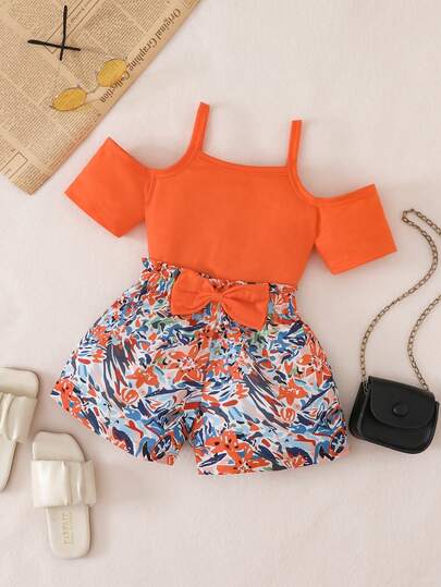 Bộ đồ mùa hè cho bé gái gồm áo thun ngắn tay trễ vai màu cam neon và quần short in hoa thắt nơ ngang eo.