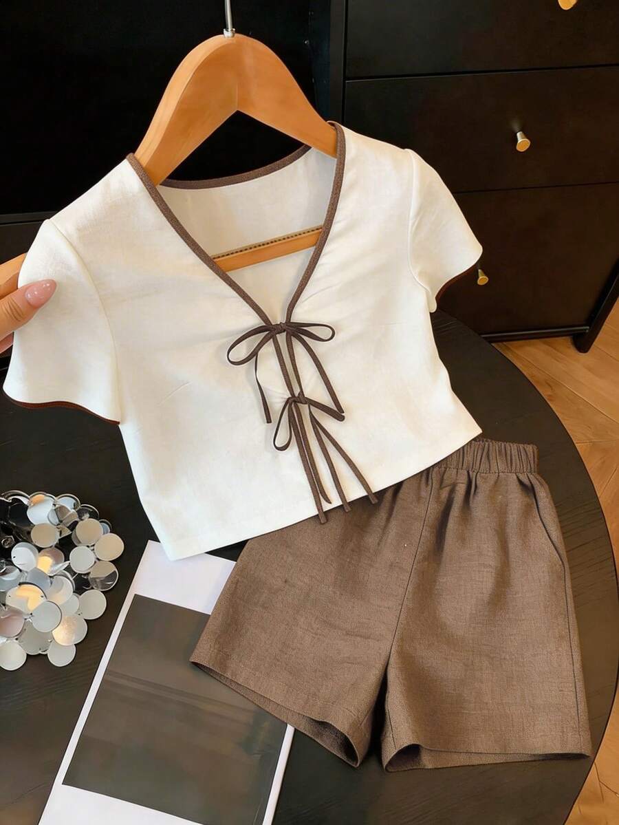 Franclia Bộ đồ nữ thường ngày gồm áo tay ngắn cổ chữ V màu trắng, chất liệu giả lanh, họa tiết chần bông, phối viền tương phản, thắt nơ tre, kết hợp với quần short màu nâu đậm, chất liệu bền chắc, thoải mái, phù hợp cho công sở. - Màu Khaki - Xem 1
