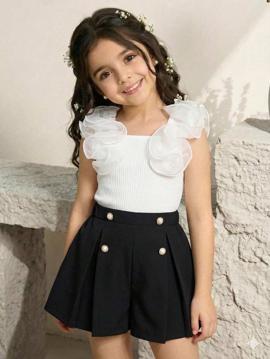 Bộ đồ hai mảnh kiểu dáng ngọt ngào và tinh nghịch gồm áo vest không tay xếp ly và áo thun dệt kim kẻ sọc ở nách, kết hợp với quần short cạp chun màu hồng, bộ quần áo trẻ em với những bông hoa trắng ba chiều tinh tế, dễ thương và thời trang, phù hợp cho sinh hoạt hàng ngày vào mùa hè.