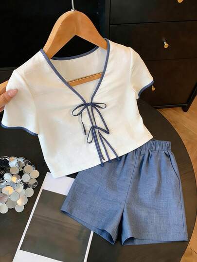 Franclia Bộ đồ nữ thường ngày gồm áo tay ngắn cổ chữ V màu trắng, chất liệu giả lanh, họa tiết chần bông, phối viền tương phản, thắt nơ tre, kết hợp với quần short màu nâu đậm, chất liệu bền chắc, thoải mái, phù hợp cho công sở.