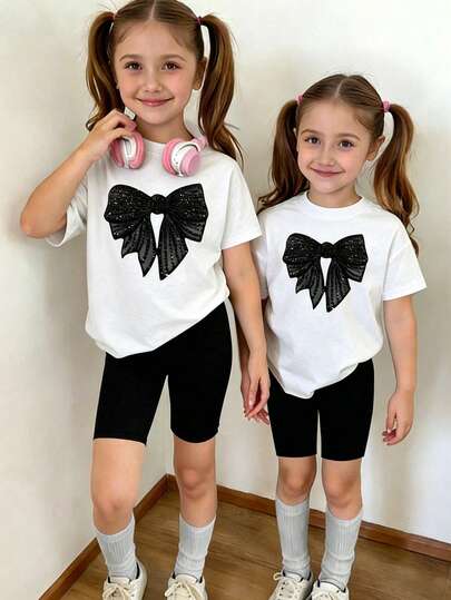 Bộ đồ cho bé gái gồm áo thun ngắn tay cổ tròn in hình nơ đính sequin lấp lánh dễ thương và quần short, thích hợp cho mùa xuân hè.