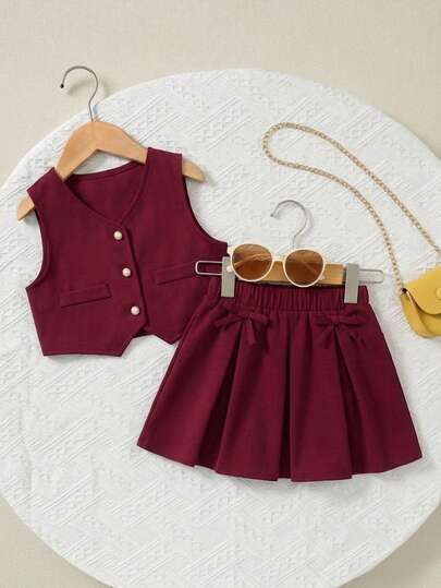 Adorable conjunto de chaleco y falda plisada para niñas con botones de perlas y detalles de lazo. Perfecto para el verano.