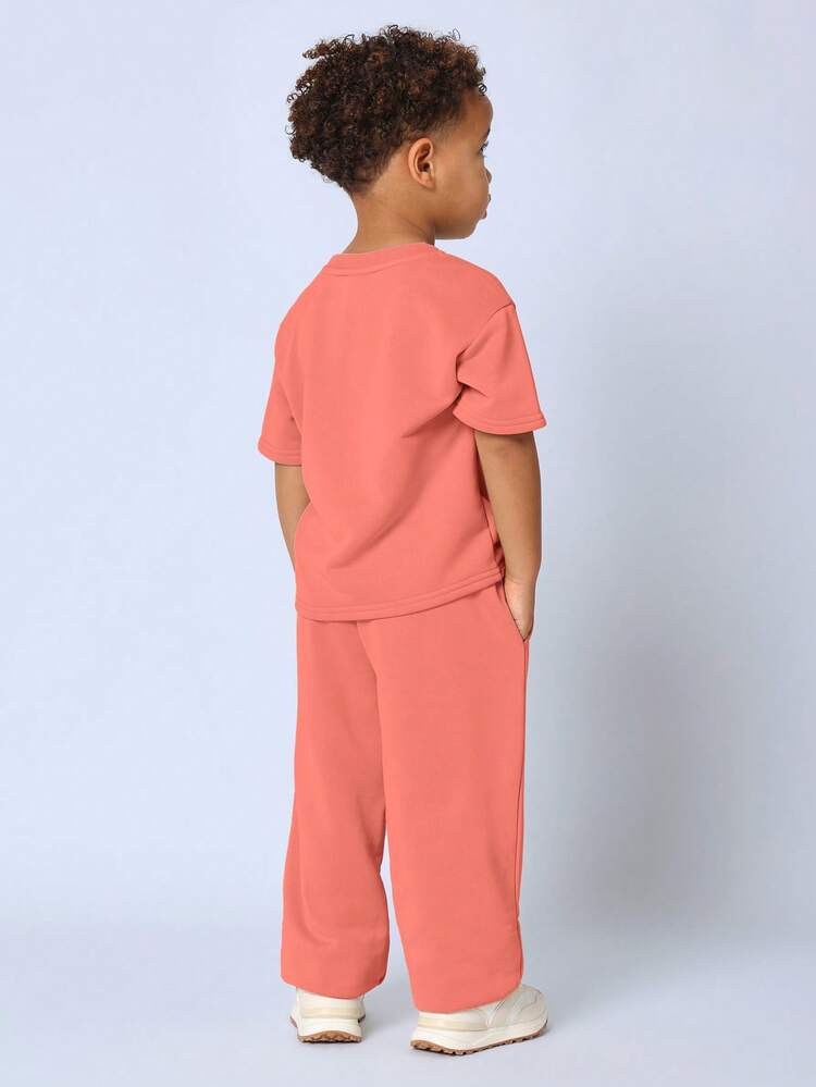 Conjunto de dos piezas oversize para niños pequeños en coral con estampado de letras blancas en la parte superior de manga corta y pantalones con cordón, ropa casual de juego
