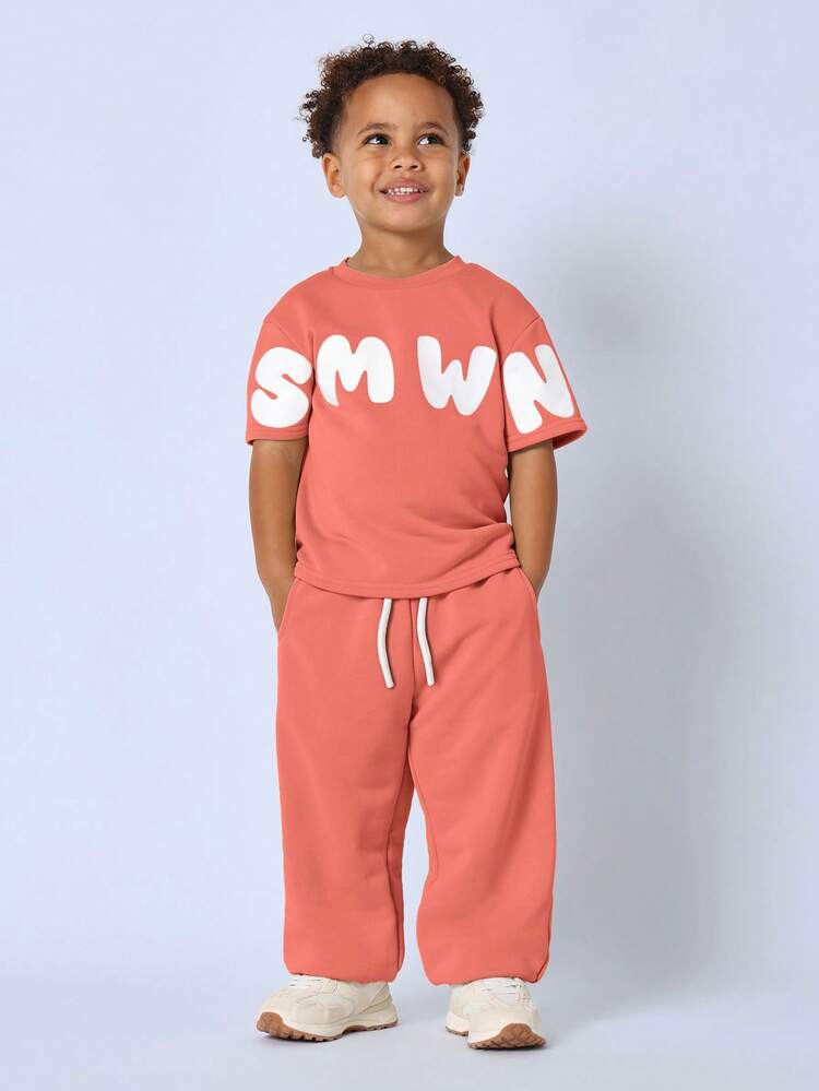 Conjunto de dos piezas oversize para niños pequeños en coral con estampado de letras blancas en la parte superior de manga corta y pantalones con cordón, ropa casual de juego