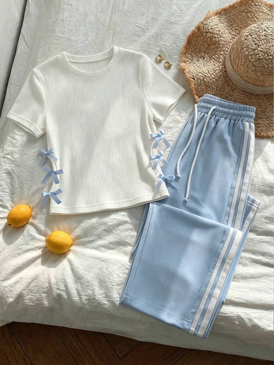 SHEIN Sparklyn 这款适合大龄女孩的两件套套装,风格时尚休闲。白色罗纹针织圆领短袖套头衫搭配粉色精梳针织宽松休闲裤。上衣侧边饰有独特的蝴蝶结,裤子则采用两条对比鲜明的白色条纹,打造运动休闲风。 - 藍色 - 查看 1