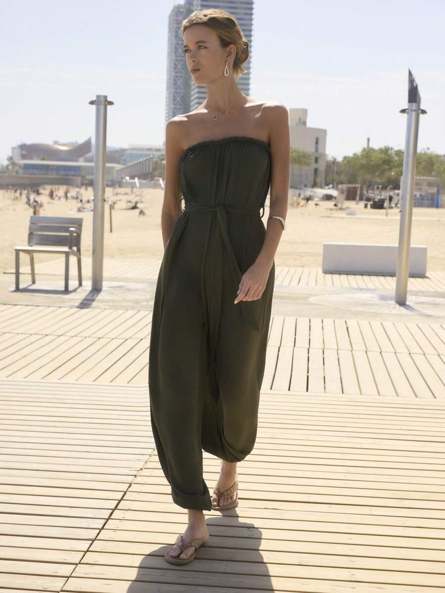 Bộ jumpsuit màu xanh ô liu không dây, hở vai, điểm nhấn là phần cổ áo được tết bím và thắt lưng vải cùng màu để tôn dáng. Hoàn hảo cho mùa hè, mùa xuân, đi biển, tiệc bể bơi, phong cách boho, lễ hội mùa hè, hoặc mặc hàng ngày. - màu xanh lá - Xem 1