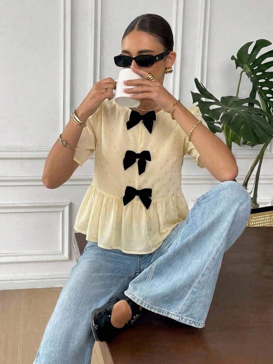 Serisse Áo sơ mi nữ cổ tròn tay ngắn, trang trí nơ và viền bèo nhún.