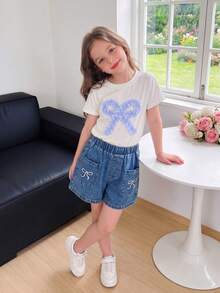 SHEIN Genkimix Kids Outfit estivo casual e carino per bambine e ragazze: top bianco a maniche corte con ricamo a fiocco, pantaloncini di jeans blu con tasche e ricami - Bianco - Visualizzare 2