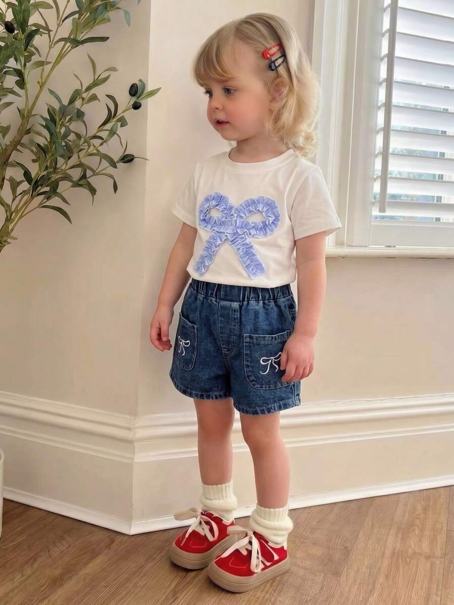 SHEIN Genkimix Kids Outfit estivo casual e carino per bambine e ragazze: top bianco a maniche corte con ricamo a fiocco, pantaloncini di jeans blu con tasche e ricami - Bianco - Visualizzare 1