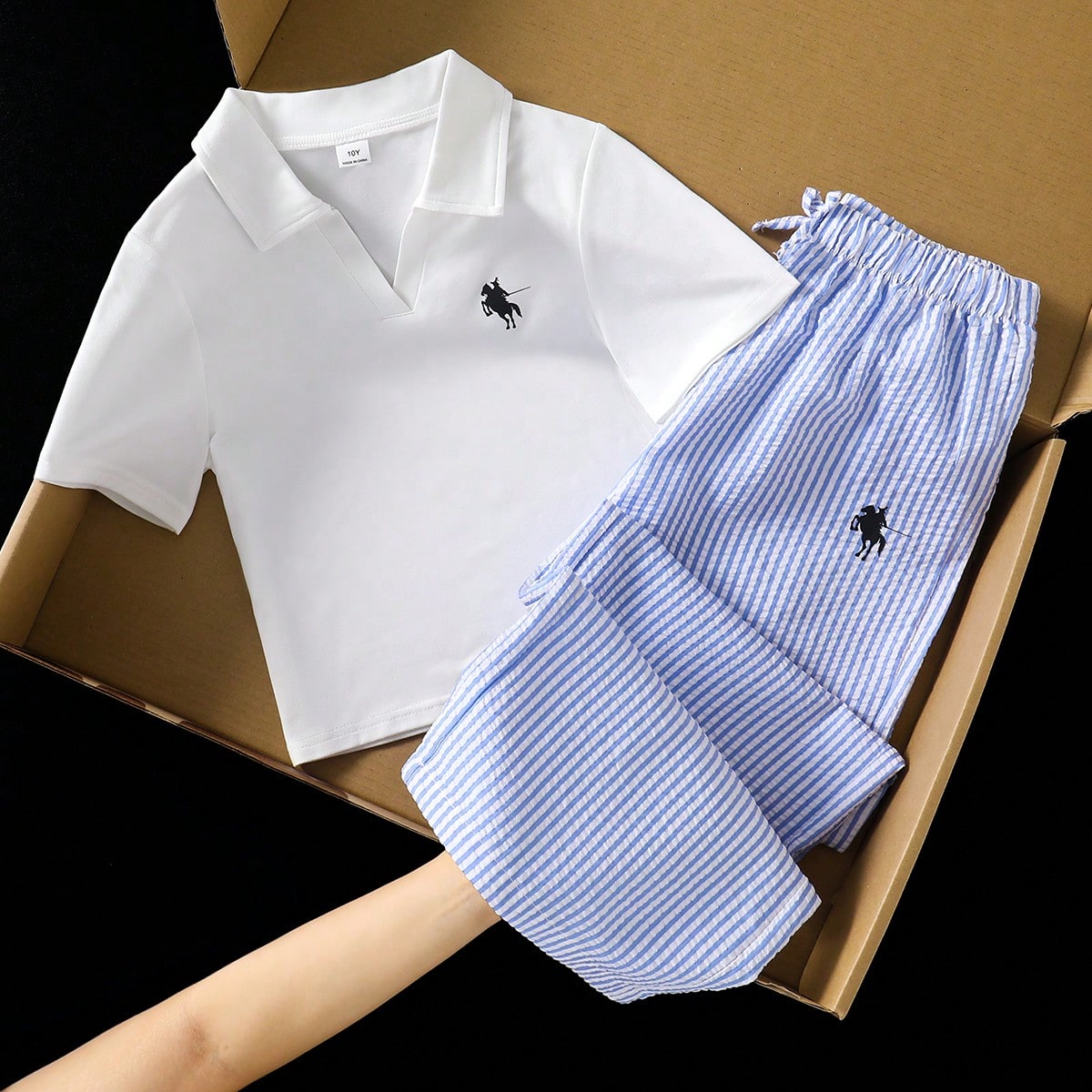 Conjunto informal de dos piezas para niñas. Una camisa polo de cuello en V emparejada con pantalones de pierna ancha de rayas verticales azul y blanc