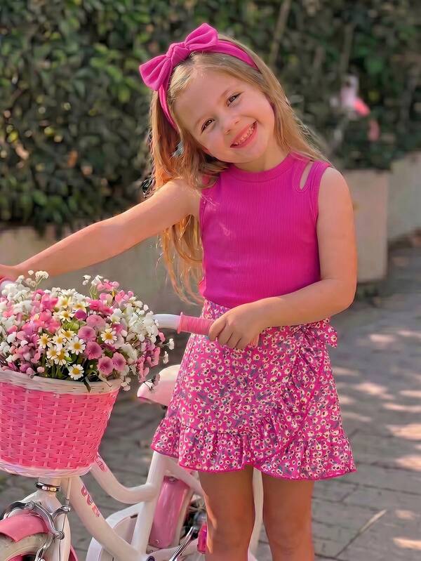 Vestido sin mangas con patchwork floral para niñas de primavera/verano, la parte superior es un top de tirantes sin mangas acanalado color fucsia con diseño de hombros descubiertos, la Bottom se combina con una falda envolvente floral del mismo color, la decoración de lazo en la cintura añade un toque juguetón, el dobladillo con volantes es alegre y suave; el estilo general es dulce y vibrante, adecuado para salidas diarias, parques de atracciones, fiestas, actividades entre padres e hijos y otras ocasiones