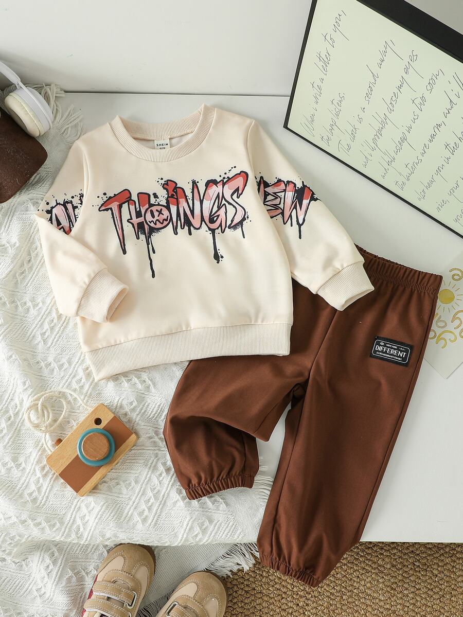 SHEIN طقم كنزة وبنطال رياضي للأطفال الصبيان من قطعتين، بلون بيج وبني مع طباعة حروف جرافيتي ورذاذ، أكمام طويلة وياقة دائرية، بقصة عادية، مناسب للخارج وللخريف