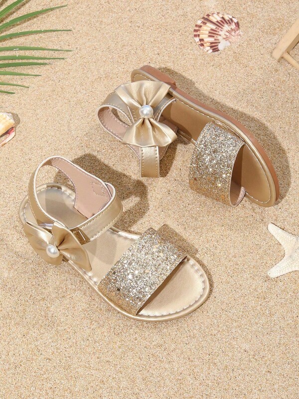 A Pair Of Cozy Pixie Spring/Summer Gold Bows Accessorize With Cute Princess-Style Flat Sandals For Baby Girls And Toddlers On Vacation