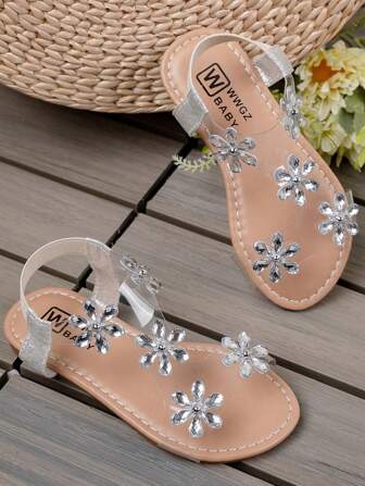 Un par de sandalias antideslizantes para niños, un éxito de en verano. La parte superior es de color marrón claro, con un diseño de cinta de PVC transparente, decorado con múltiples flores de rhinestone plateadas, con un brillo delicado.